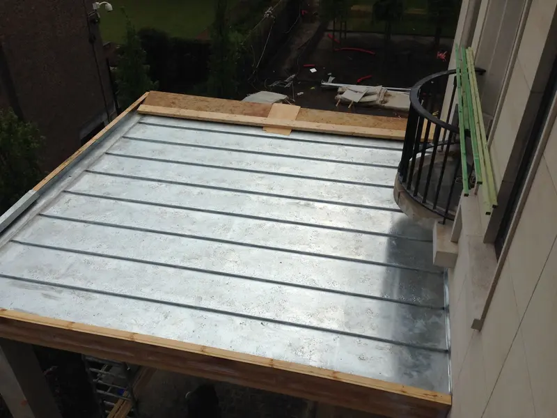 Toiture en zinc à joint debout vue de dessus, joints parallèles, rive en bois et balcon de la façade voisine.
