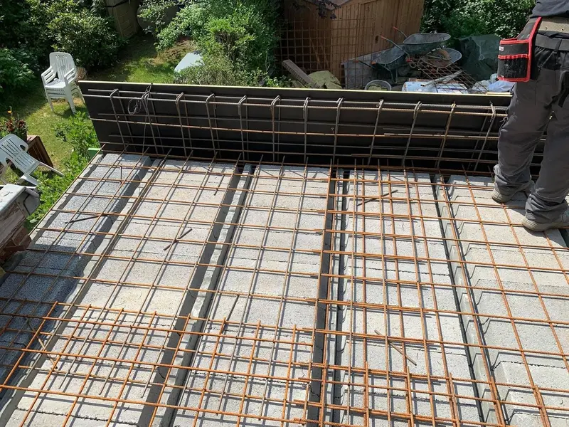 Treillis d’armature sur un plancher à hourdis avec coffrage de rive, le jardin et la façade existante à l’arrière.