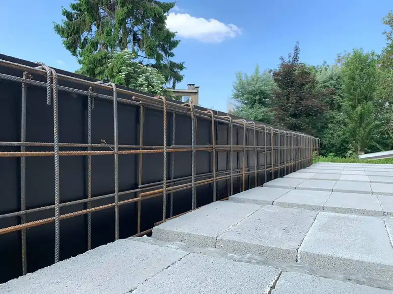 Cage d’armature et coffrage noir d’un mur de soutènement, en ligne droite le long d’une terrasse en béton fraîchement coulée.