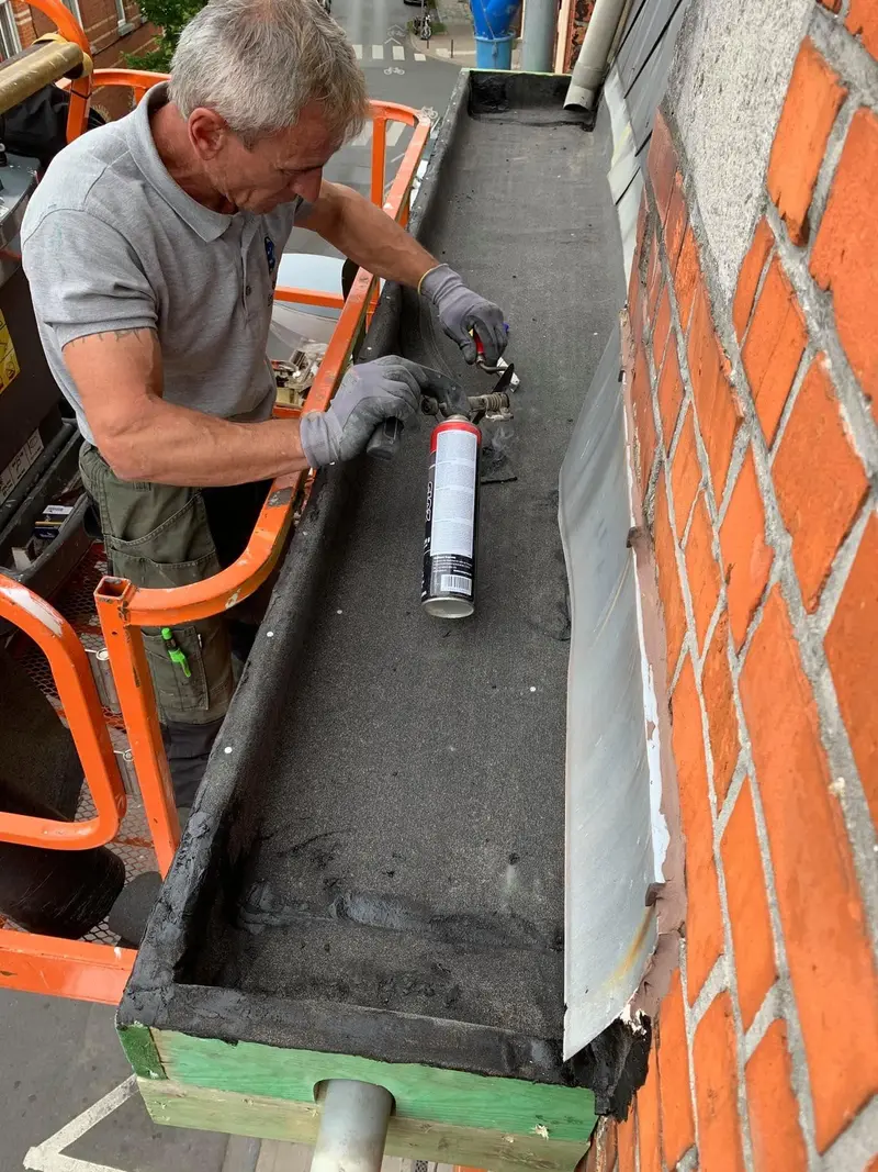 Depuis la nacelle d’une élévatrice, la finition de rive de toiture est soudée au chalumeau le long de la façade.