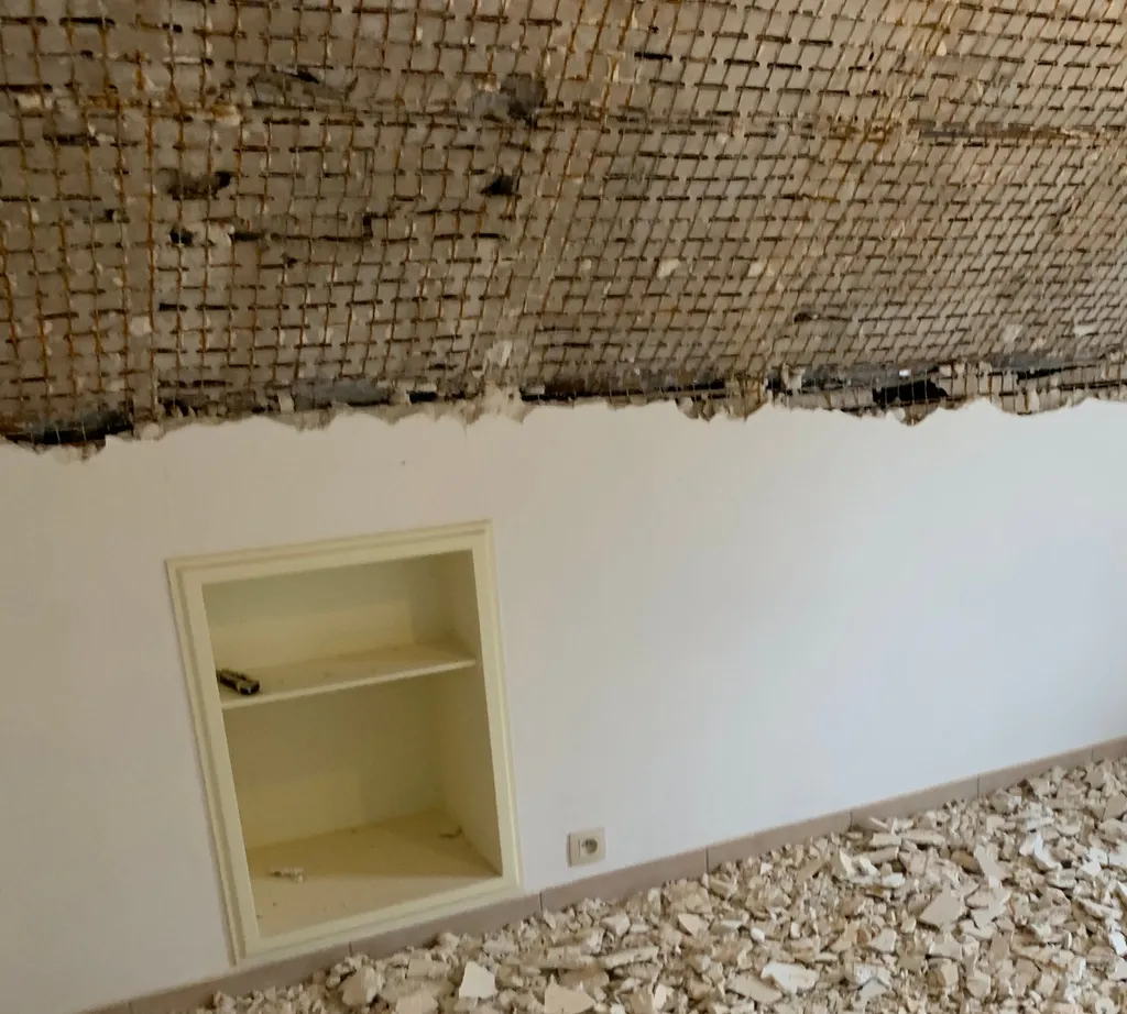 Plafond démoli jusqu’au lattis, gravats de plâtre au sol.