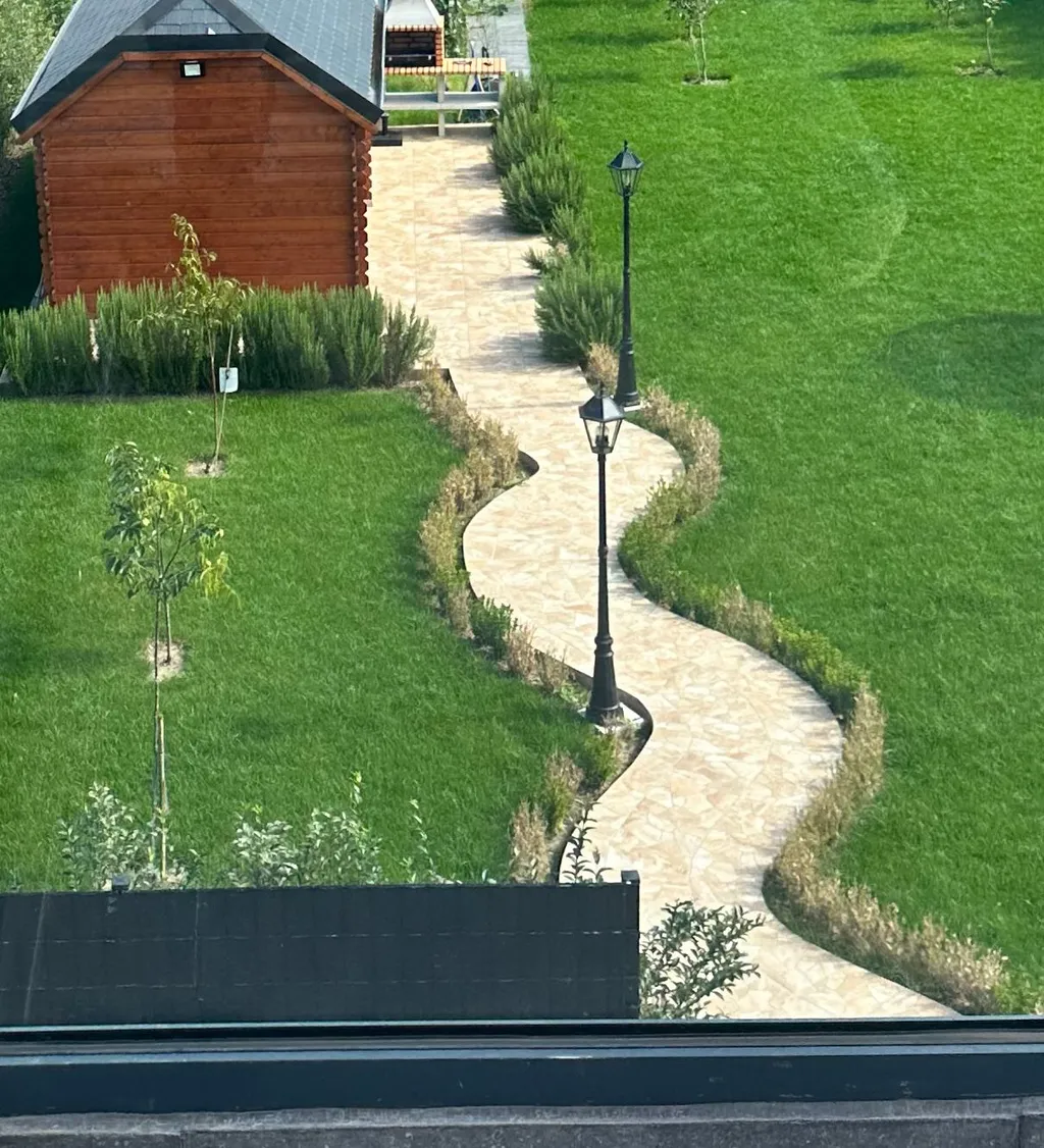 Jardin aménagé avec le même sentier en pierre naturelle, pelouse et massifs.
