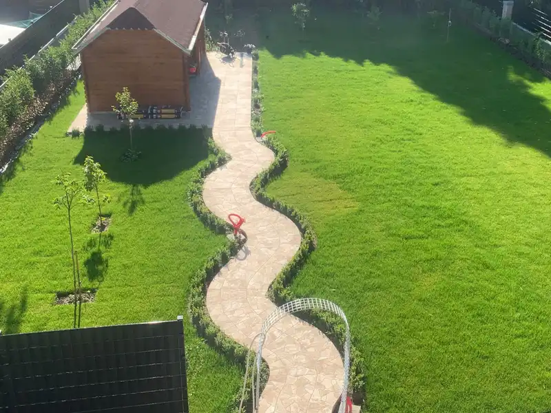 Le jardin vu de l’étage : gazon, chemin sinueux en pierre naturelle, haies et abri de jardin.