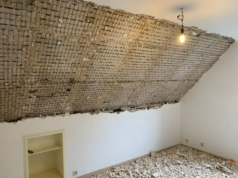 Une pièce dont le plafond a été démoli jusqu’au lattis de roseau, avec les gravats d’enduit couvrant tout le sol.