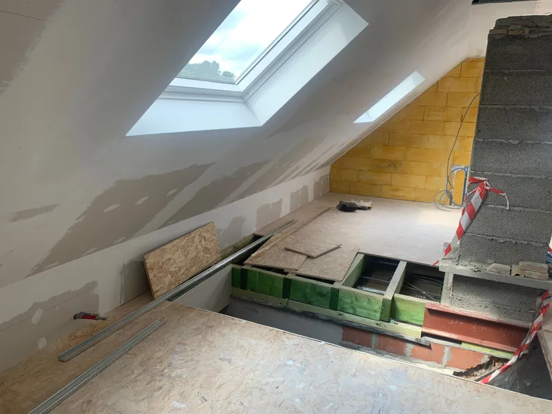 Combles aux rampants enduits, avec fenêtres de toit et une structure de plancher ouverte : solives en bois posées sur une poutre en acier.